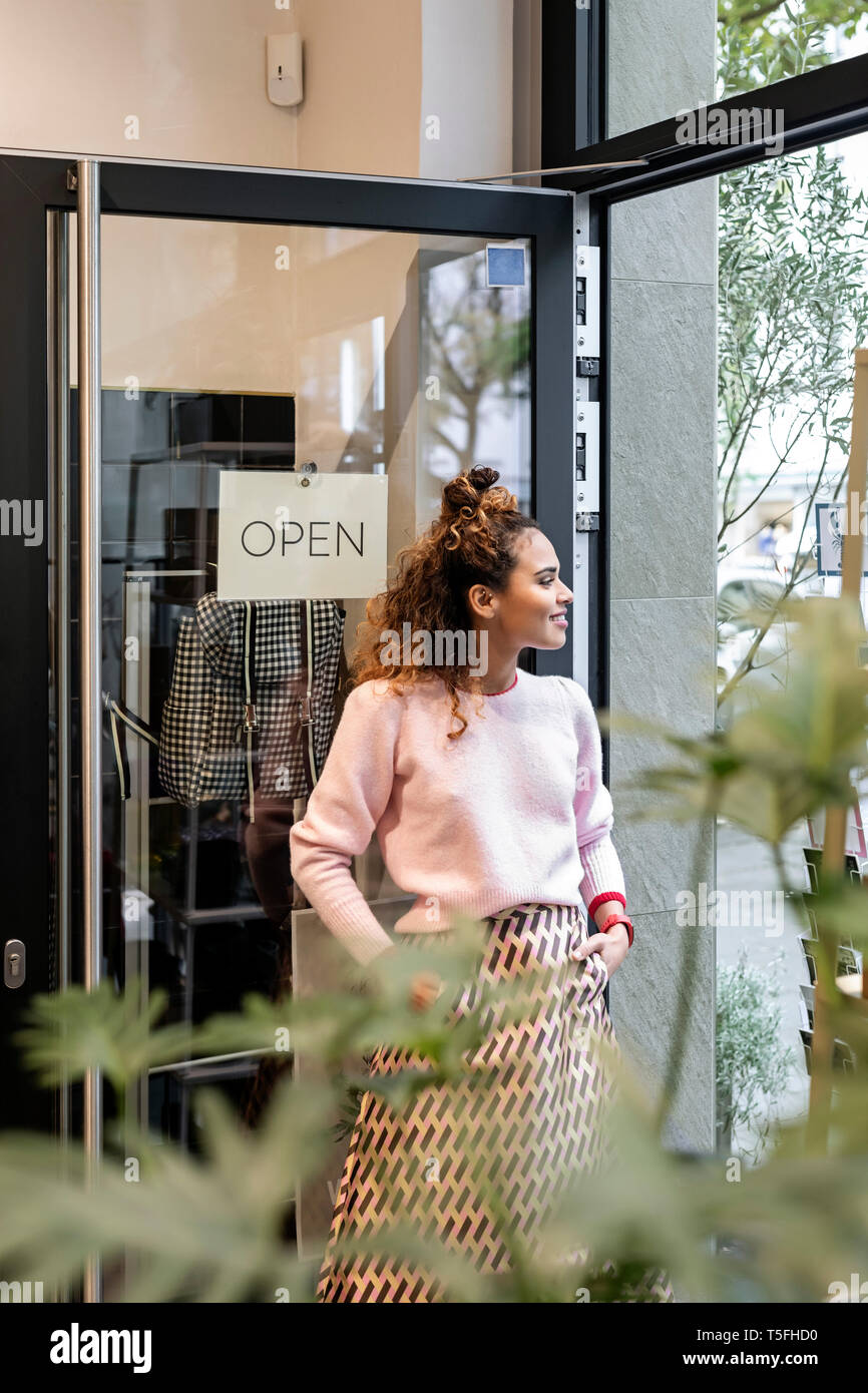 Young woman standing in open shop door, smiling Stock Photo - Alamy