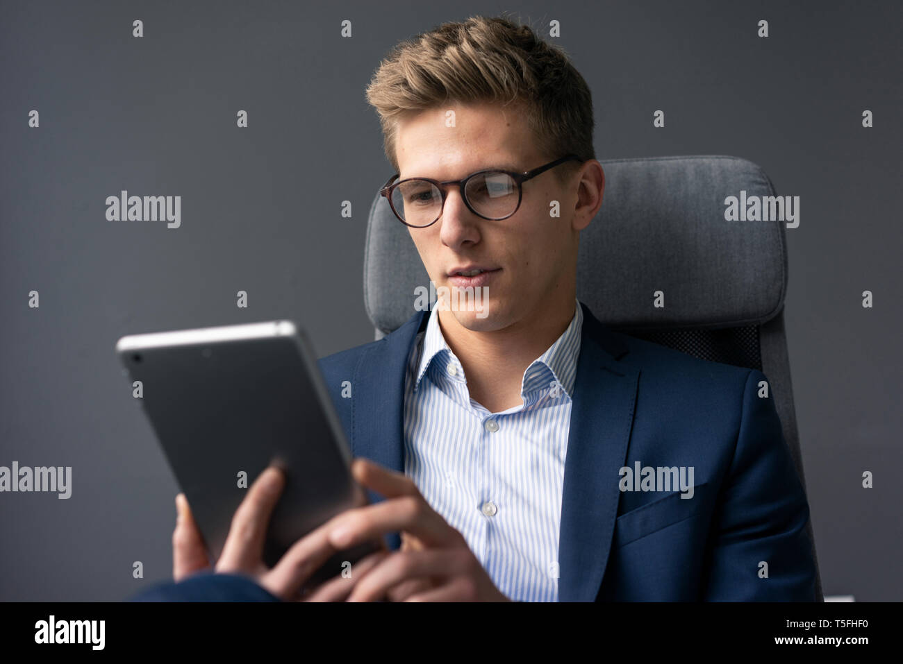 Young businessman sitting on office chair using tablet Stock Photo