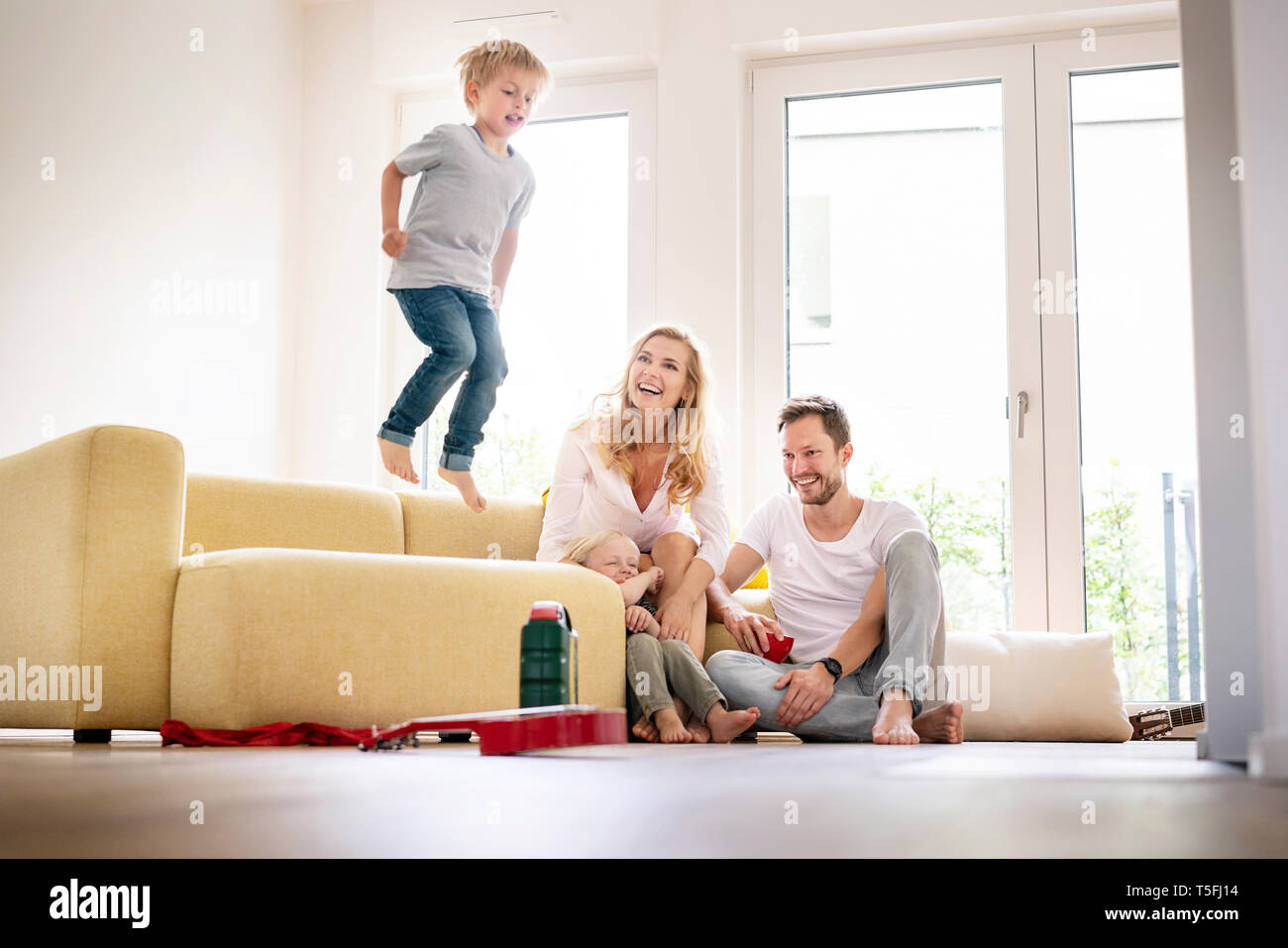 Happy family moving into their new home, boy jumping on couch Stock