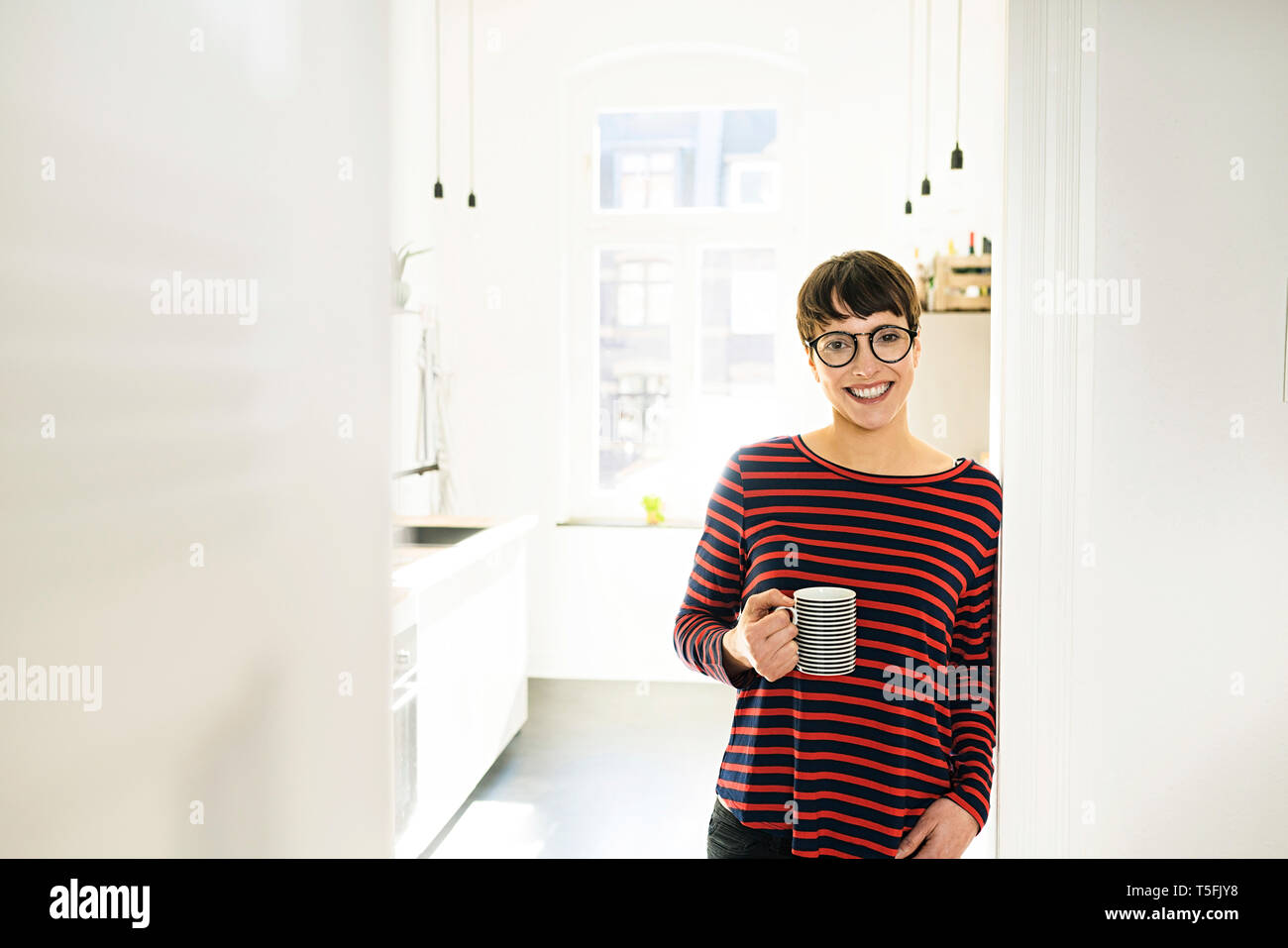 Confident short-haired woman with coffee mug leaning against door case Stock Photo