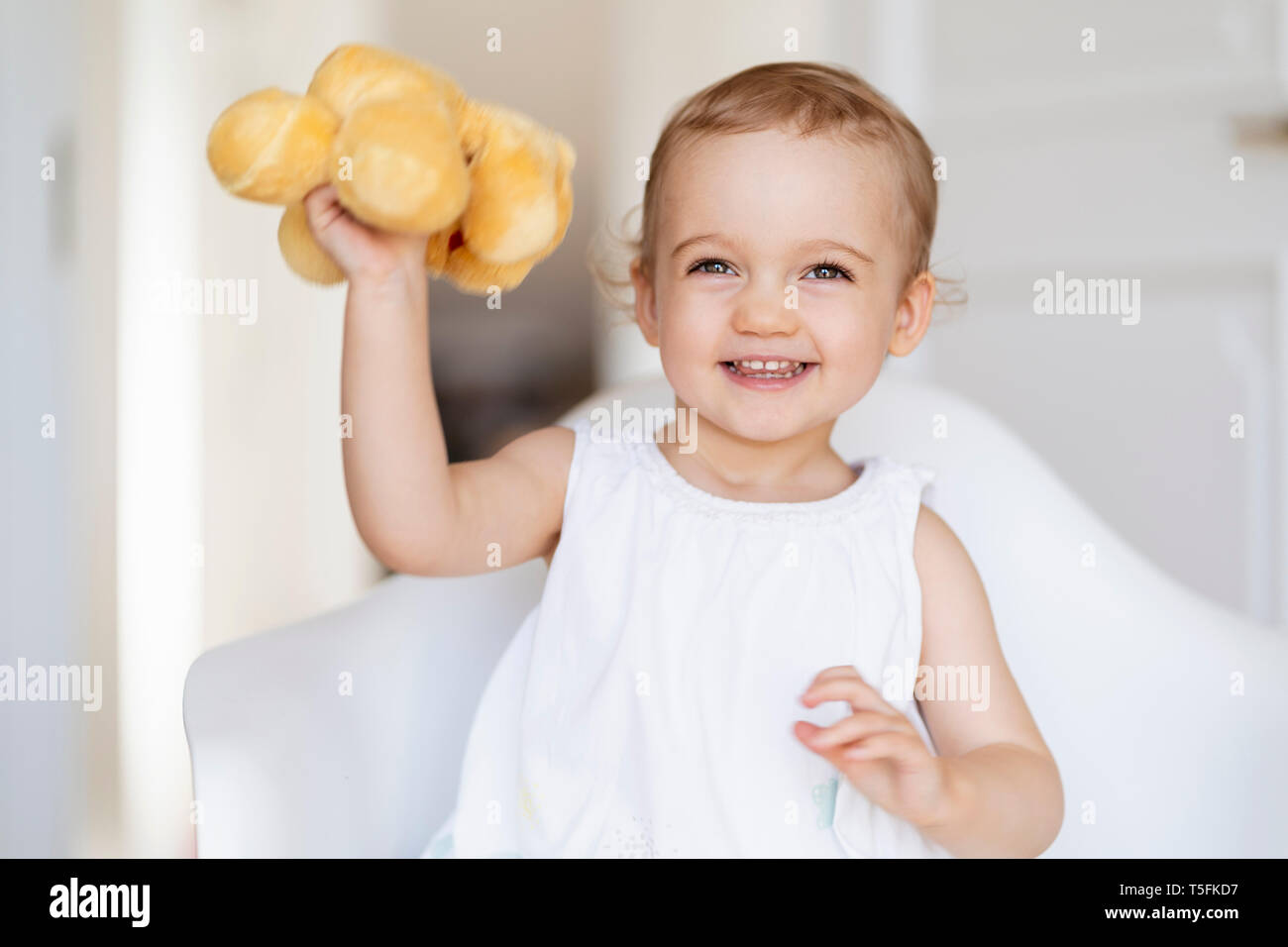 Portrait of smiling toddler girl sitting on a chair holding soft toy Stock Photo