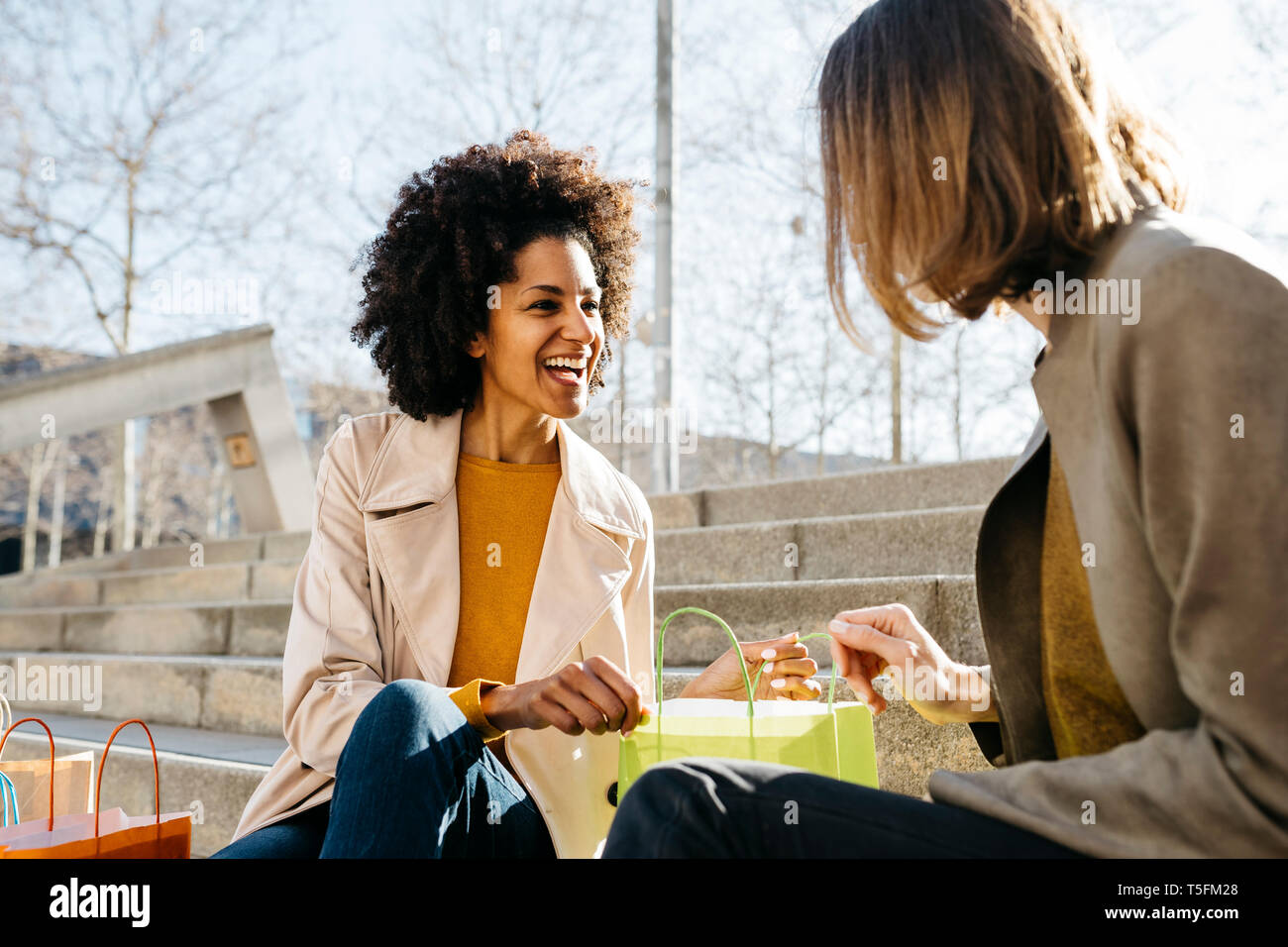 Two happy women with shopping bags sitting on stairs checking the purchase Stock Photo