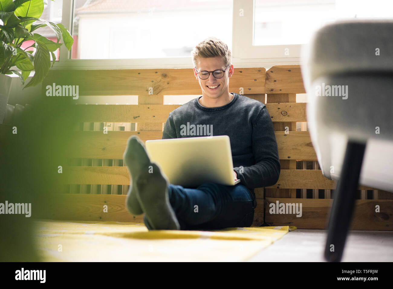 Smiling young man sitting on the floor using laptop Stock Photo