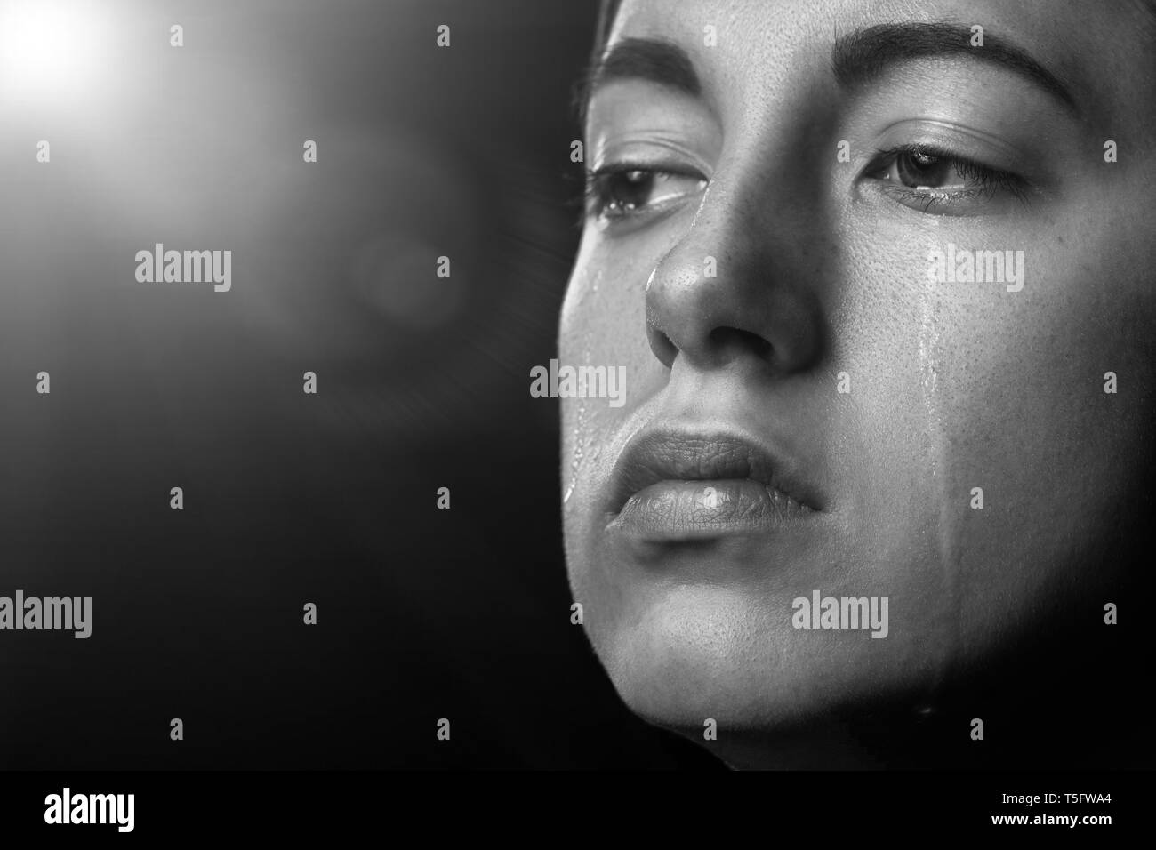 sad woman crying on black background with light rays, closeup portrait, monochrome Stock Photo