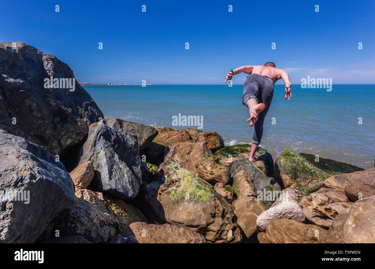 Young caucasian man practices yoga on the rocks by the beach. Outdoor yoga warrior 3 variation pose Stock Photo