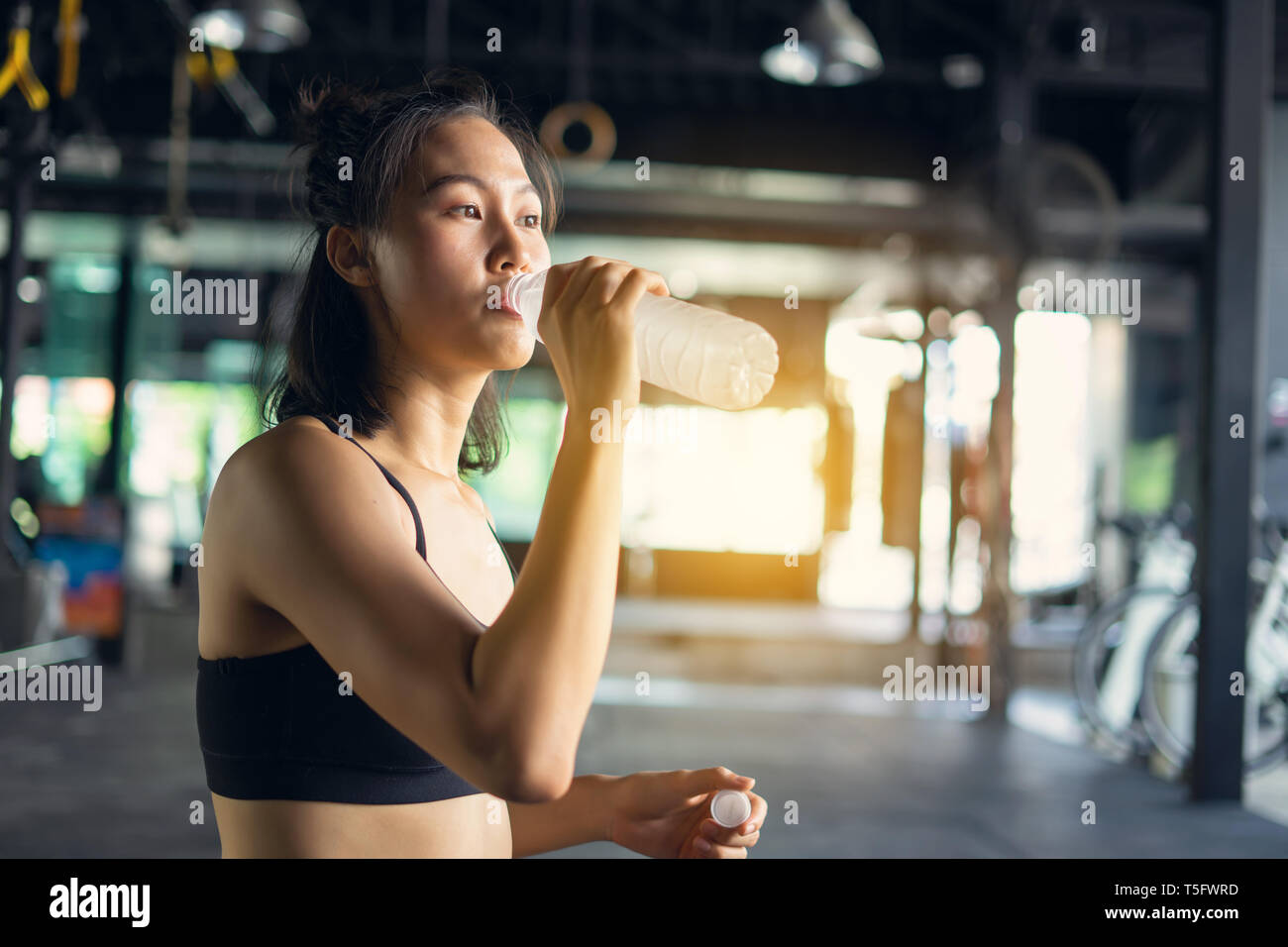 Sporty beautiful woman exercising relax and drink water with training equipment blurry background, Healthy life and gym exercise equipments and sports Stock Photo