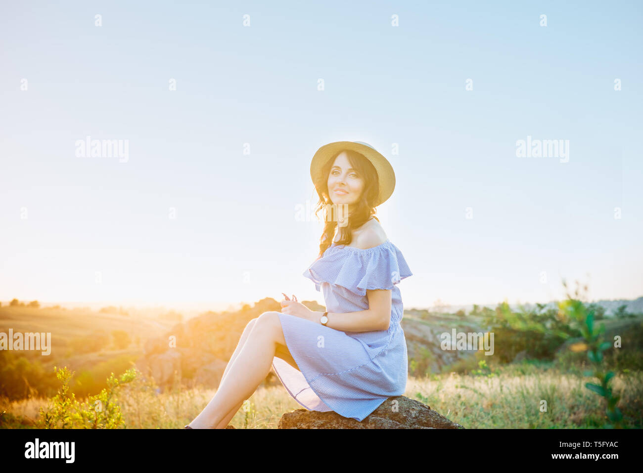 Portrait of young woman in blue romantic dress and straw hat in sun ...