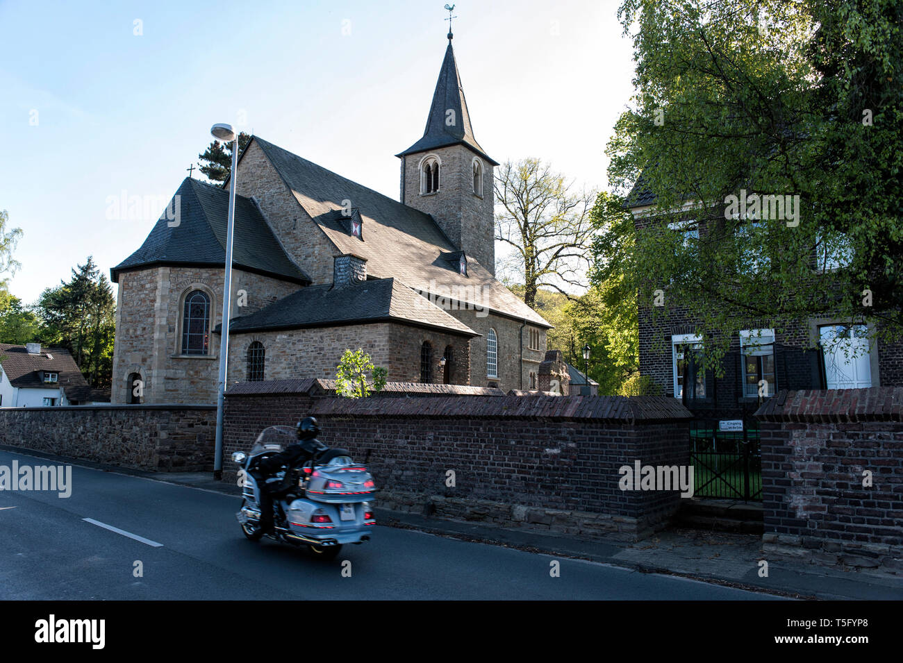 An der Kirche St. Laurentius in Mülheim Mintard faehrt ein Motoradfahrer mit einer grossen Maschine vorbei. Stock Photo