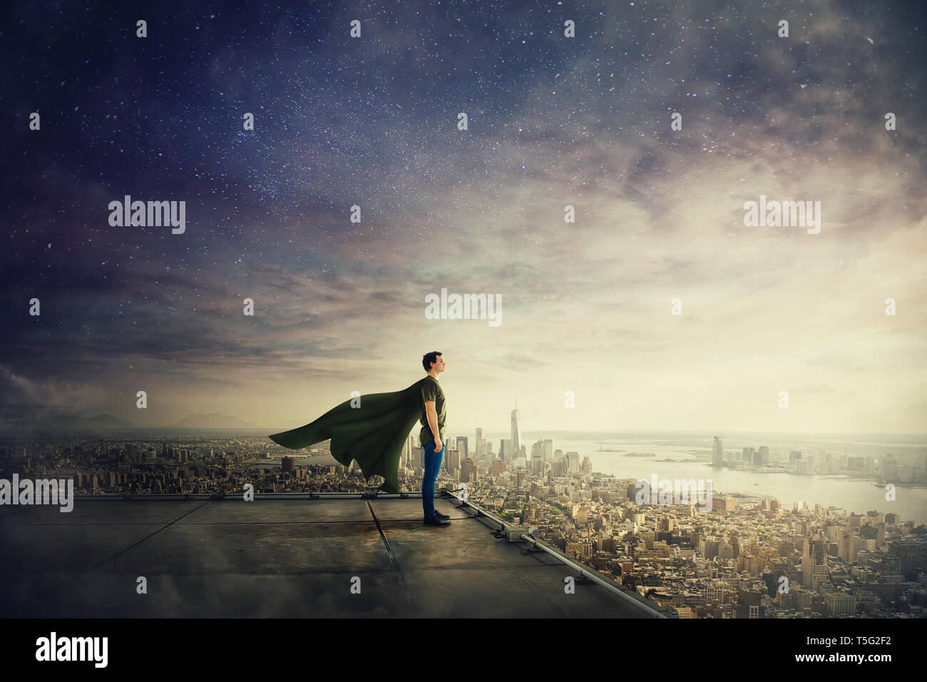Surreal view of confident superhero with cape stands on the rooftop looking over city horizon. Ambition and business success concept. Leadership hero  Stock Photo
