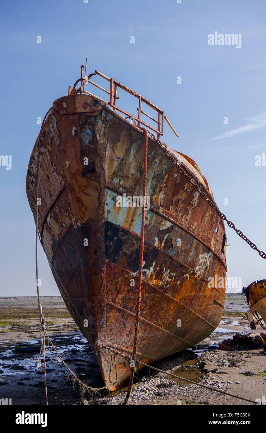 A ship wrecked fishing boat aground and abandoned rusting away on the shore line at Rampside in Cumbria Stock Photo
