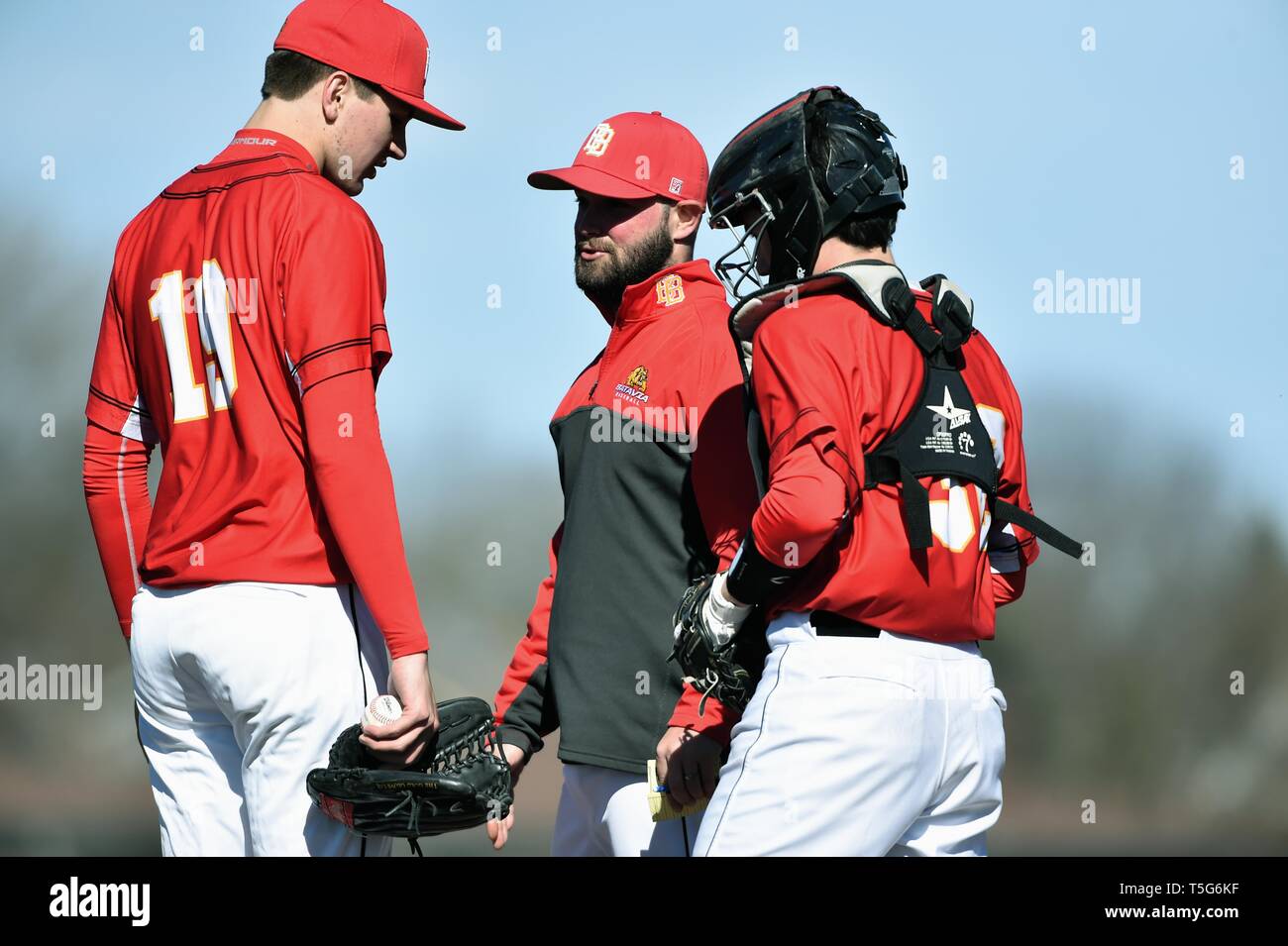Coach visits the mound to talk with his pitcher as the catcher listens to the discussion. USA. Stock Photo