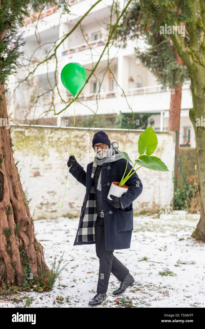 Smiling mature man with green balloon and potted plant in winter Stock Photo