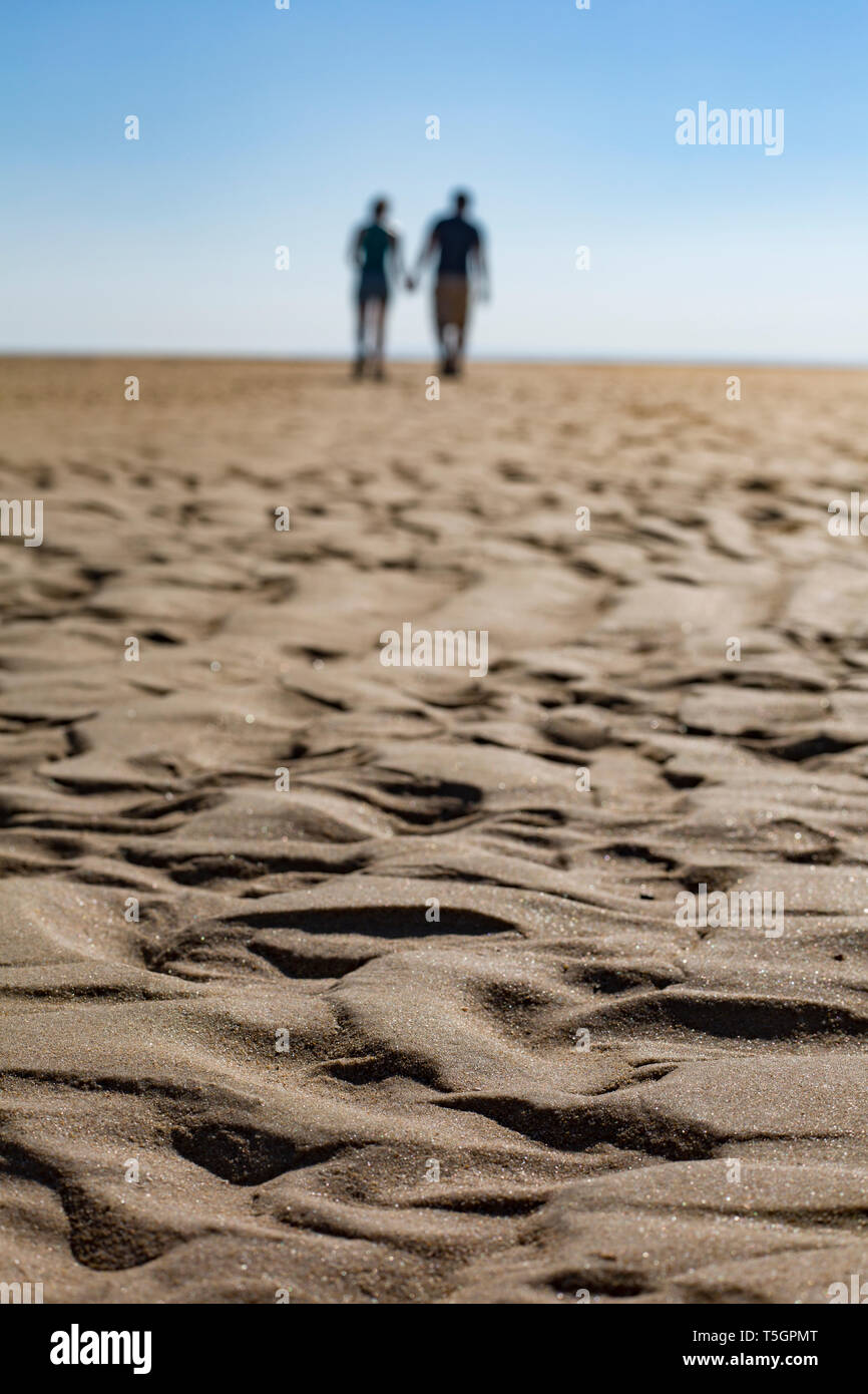 Wave pattern on the beach with silhouette of couple walking hand in ...