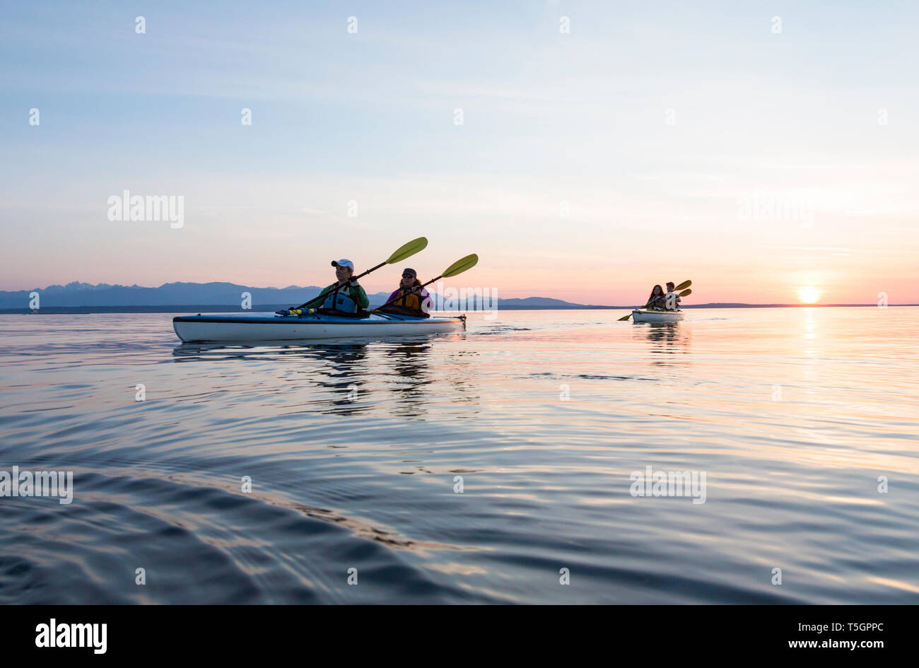 Group of people friends sea kayaking together at sunset in beautiful nature. Active outdoor adventure sports. Stock Photo