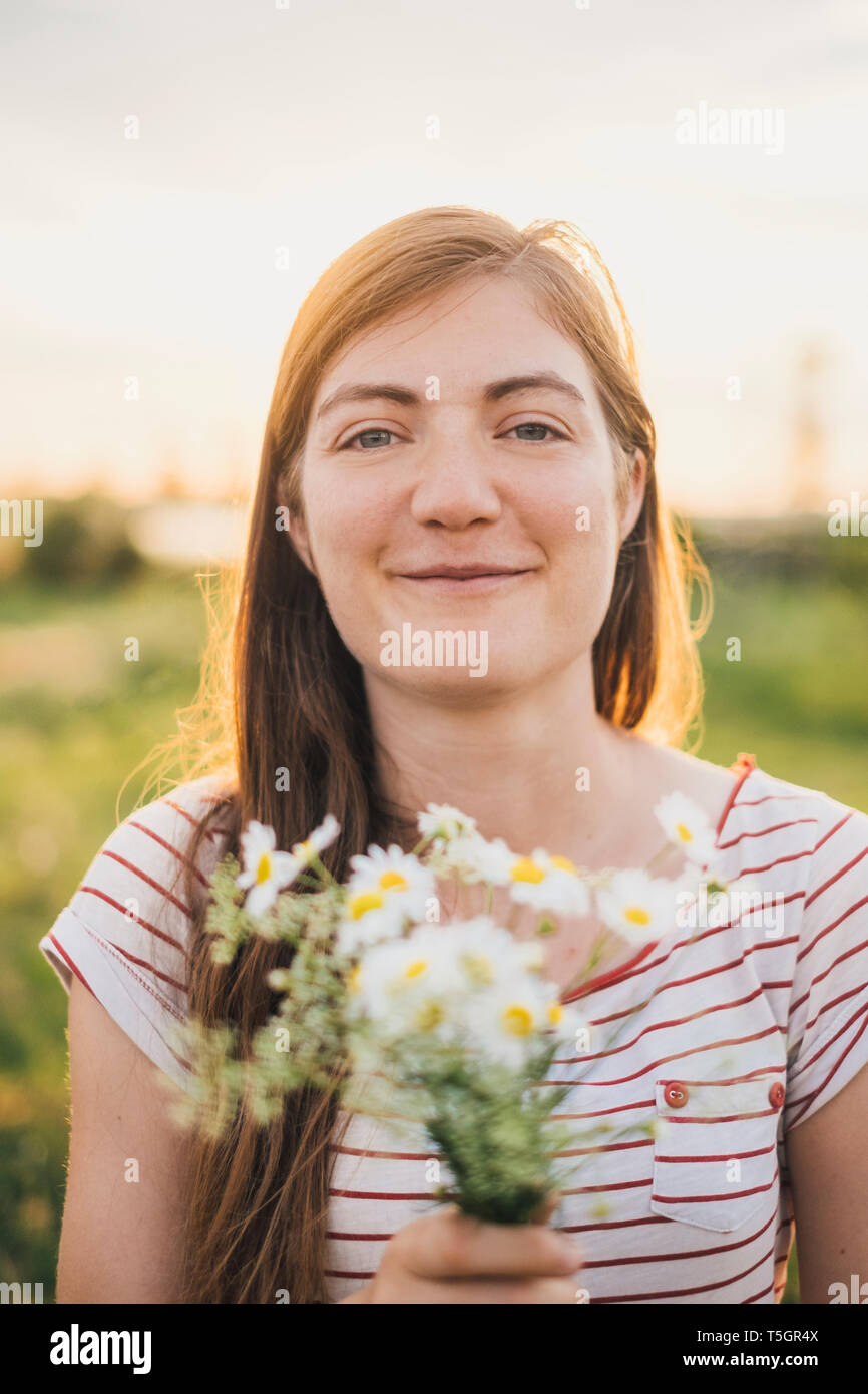 Portrait of smiling young woman holding bunch of picked wildflowers Stock Photo