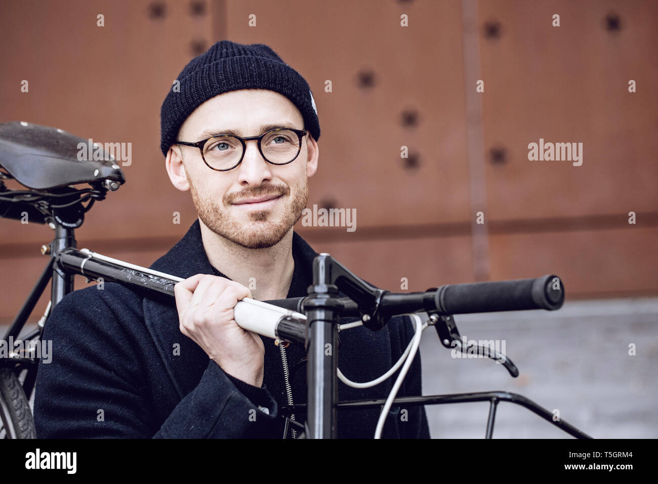 Man with beanie hat carrying his bicycle Stock Photo