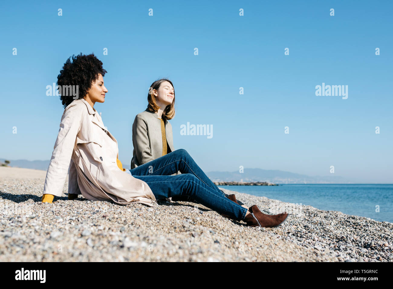 Two friends sitting on the beach enjoying leisure time Stock Photo