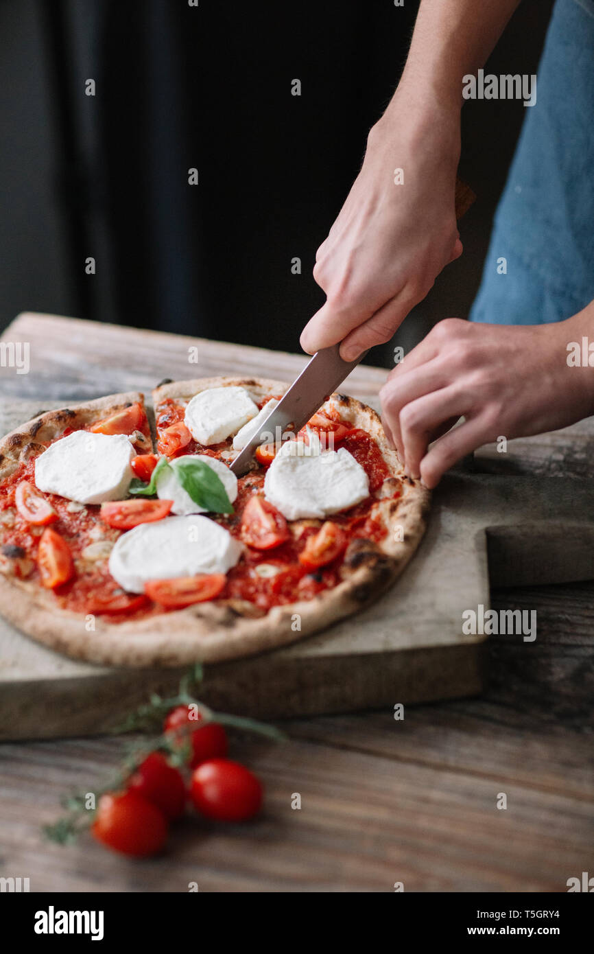 Young man preparing pizza, cutting pizza Stock Photo