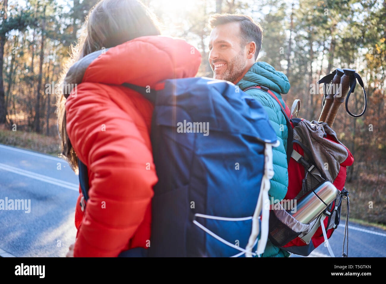 Happy couple walking along road in the woods during backpacking trip Stock Photo