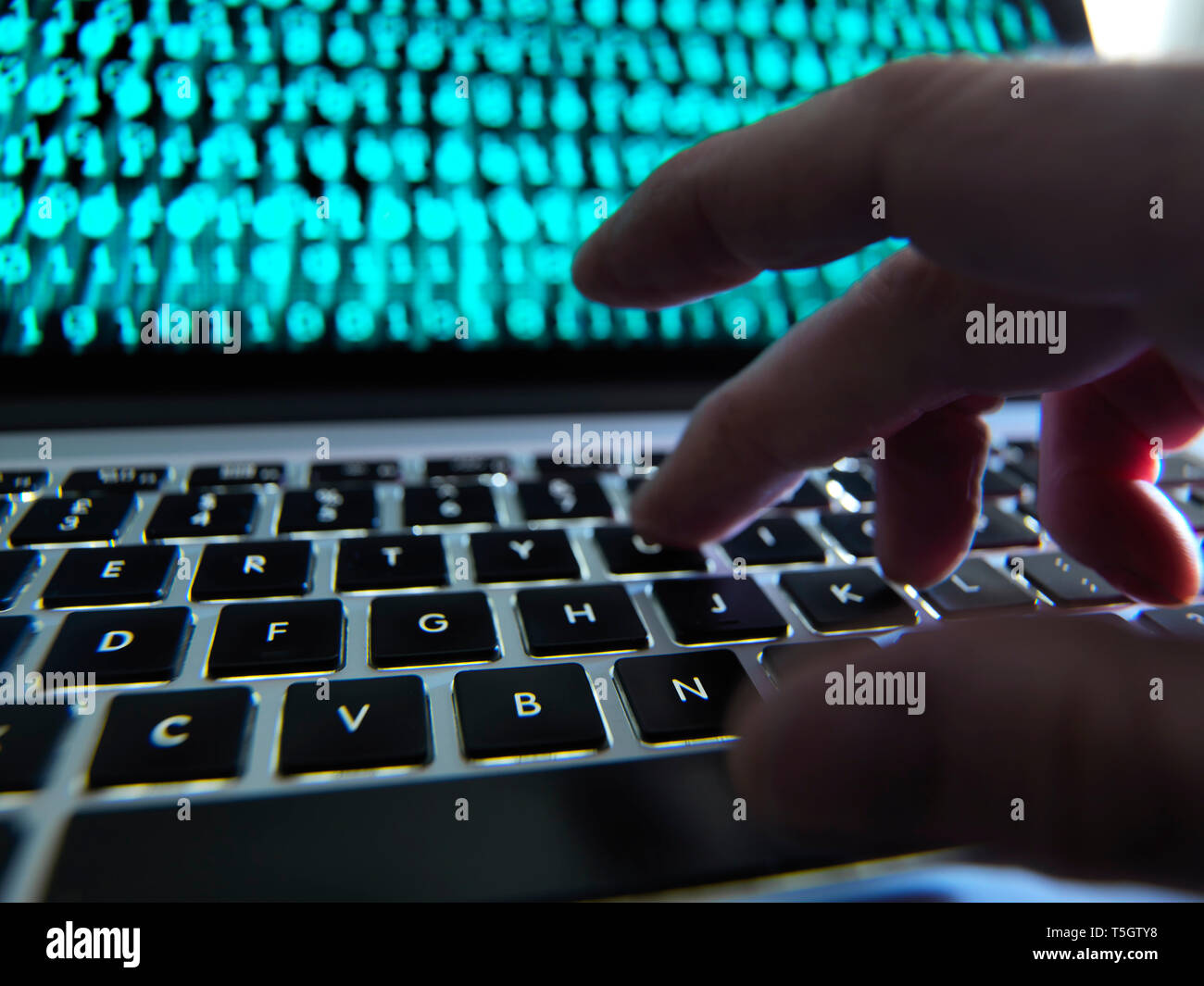 Hacker coding a computer virus infecting a laptop Stock Photo