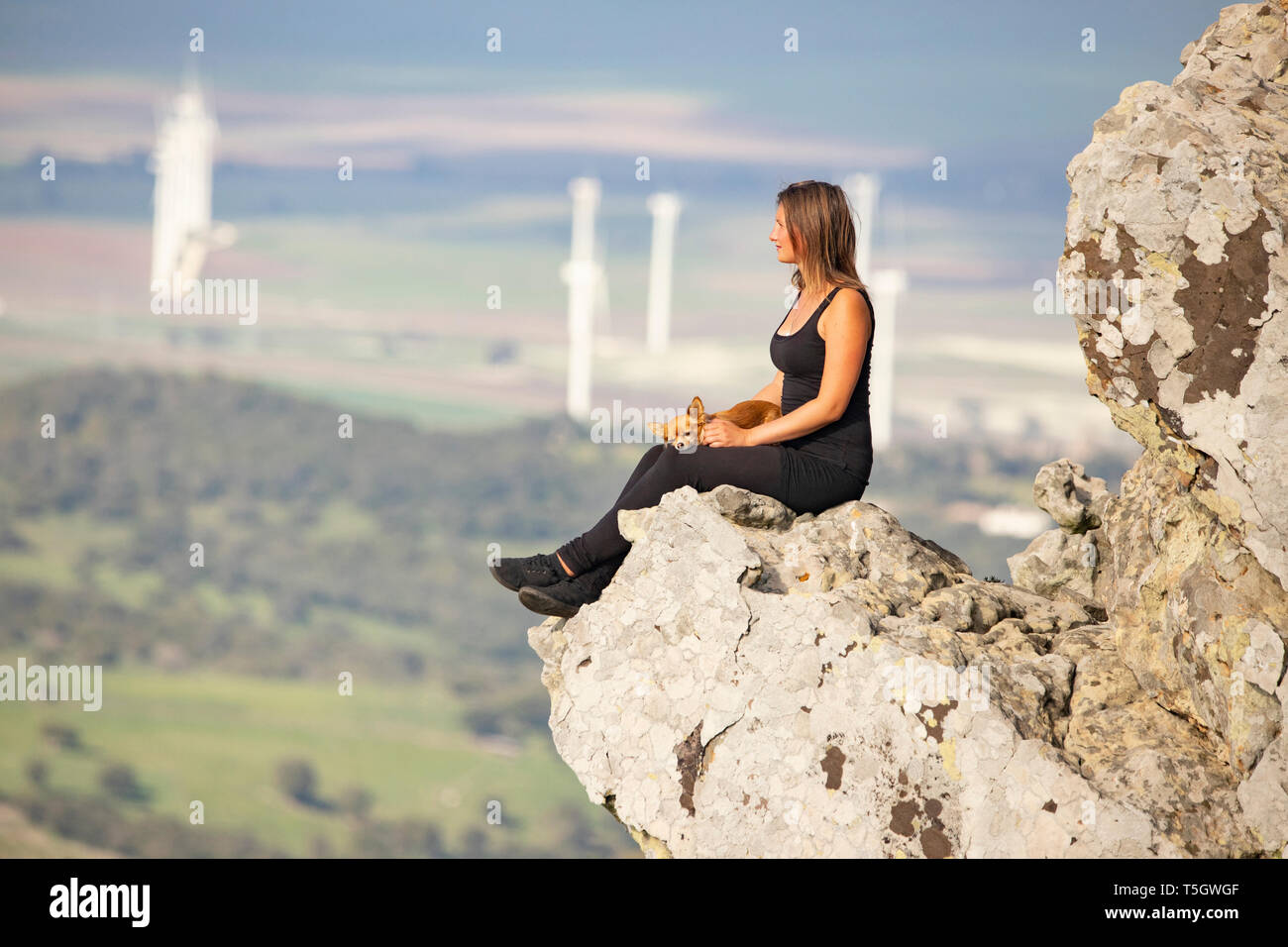Young woman with lap dog sitting on rock, looking at distance Stock Photo
