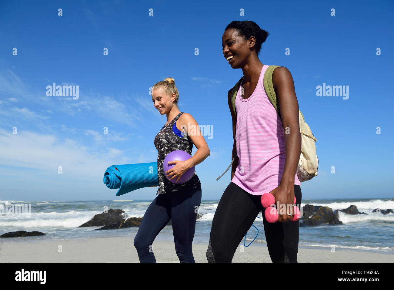 Two happy women with fitness equipment walking on the beach Stock Photo