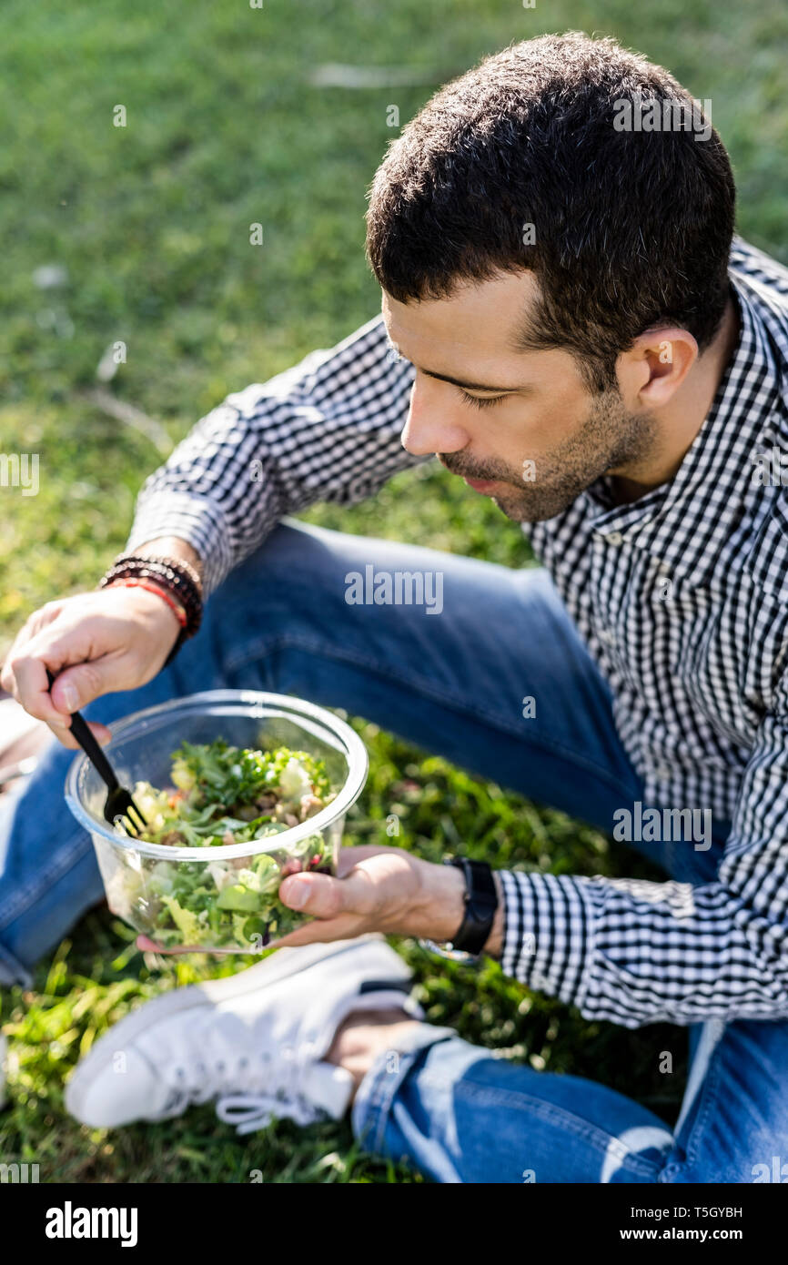 Man sitting on a meadow in city park eating mixed salad Stock Photo