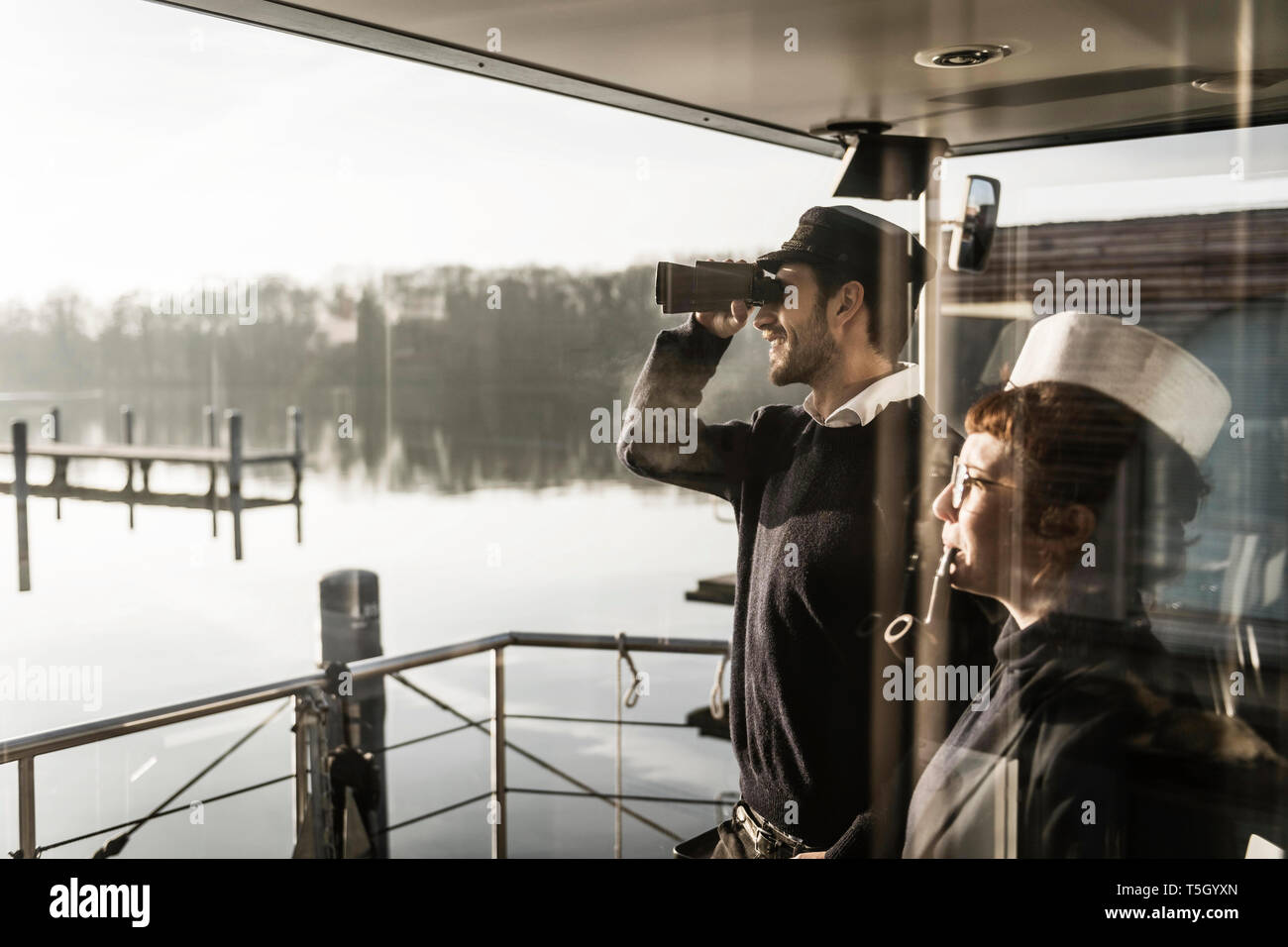 Colleagues working on a houseboat, watching surroundings with binoculars Stock Photo