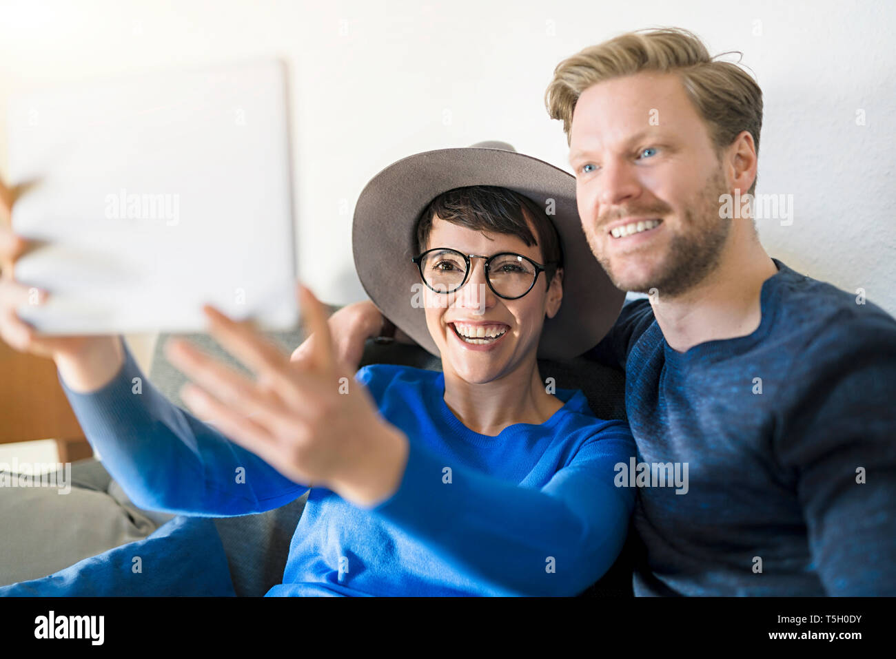 Happy casual couple taking a selfie with tablet in living room Stock
