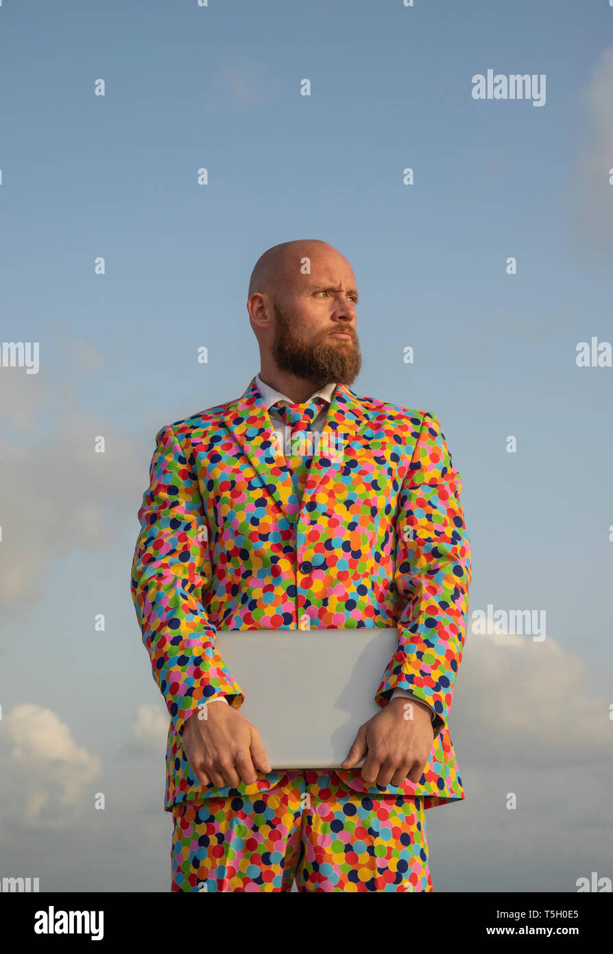 Portrait of bald man with beard  wearing suit with colourful polka-dots holding laptop Stock Photo