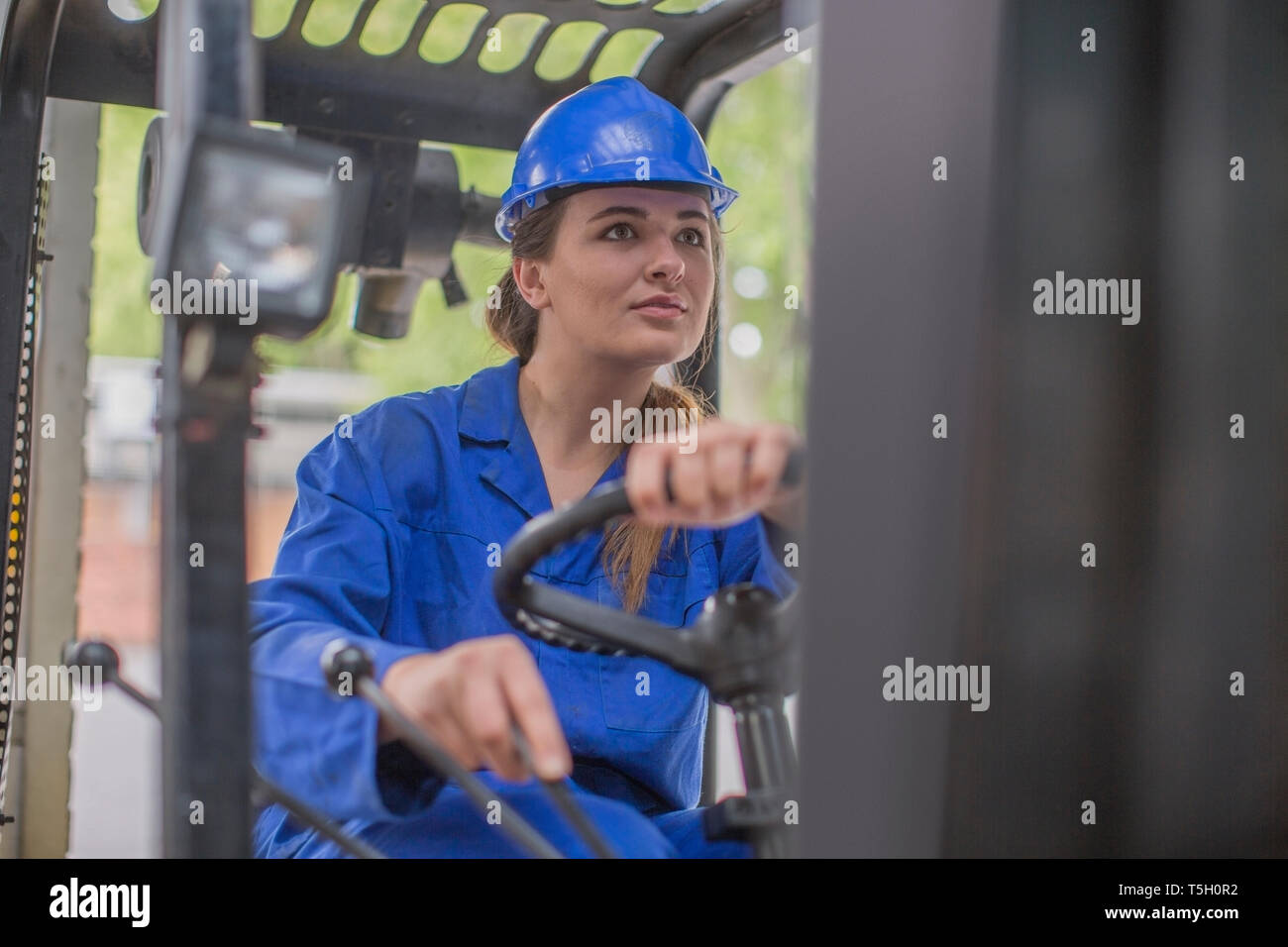 Woman wearing hard hat driving forklift in factory Stock Photo Alamy