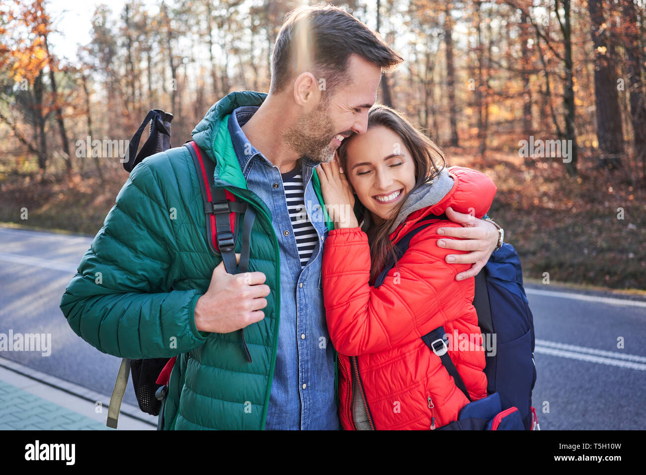 Happy couple embracing on a road in the woods during backpacking trip Stock Photo