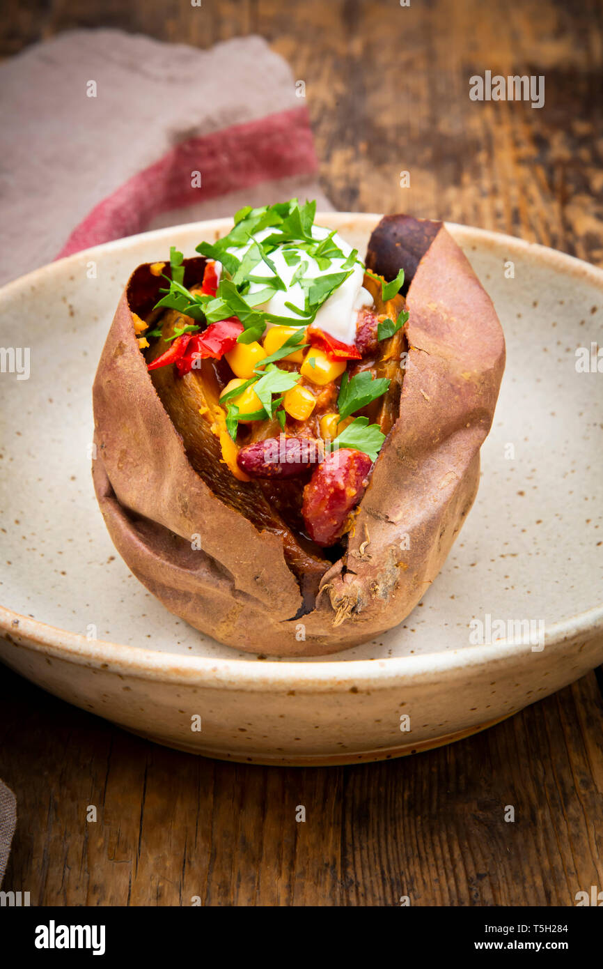 Sweet potato kumpir with chili con carne, sour cream and coriander Stock Photo