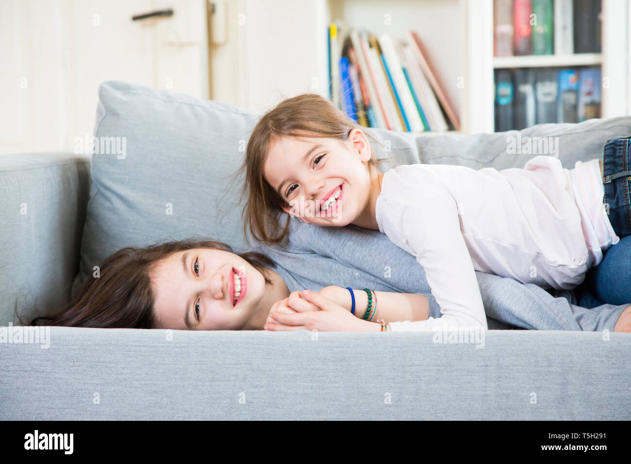 Portrait of two happy sisters cuddling on the couch Stock Photo