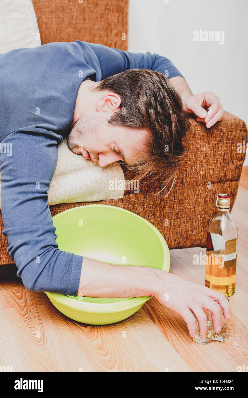 Drunken man is sleeping on sofa with bowl under bed. Acohol addiction. Stock Photo