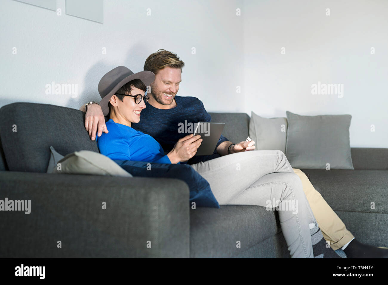 Happy casual couple relaxing on couch using tablet Stock Photo