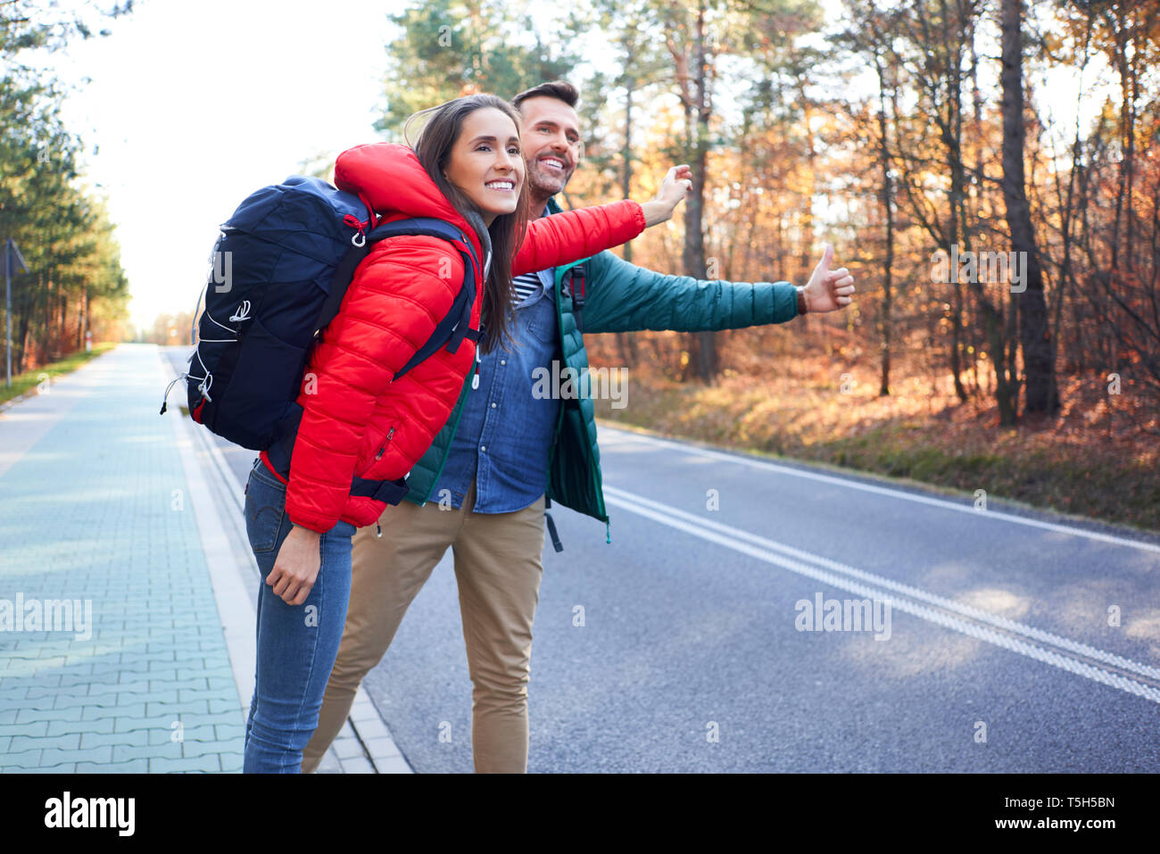 Happy couple hitchhiking road in the woods during backpacking trip Stock Photo