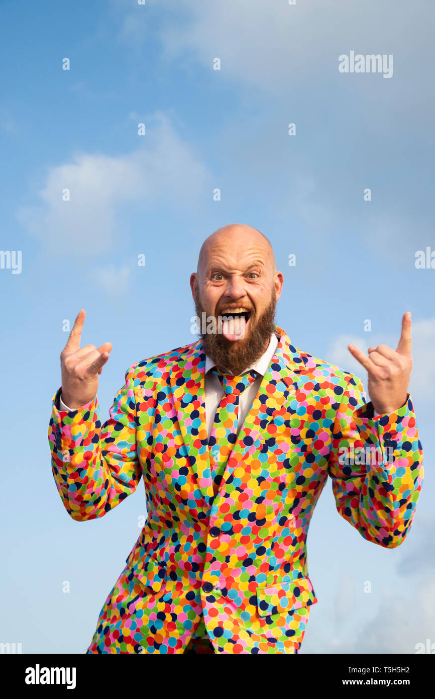 Portrait of bald man with beard  wearing suit with colourful polka-dots sticking out tongue Stock Photo