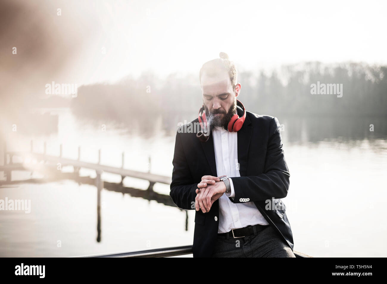 Businessman standing on a housebpat, smoking pipe, checking time Stock Photo