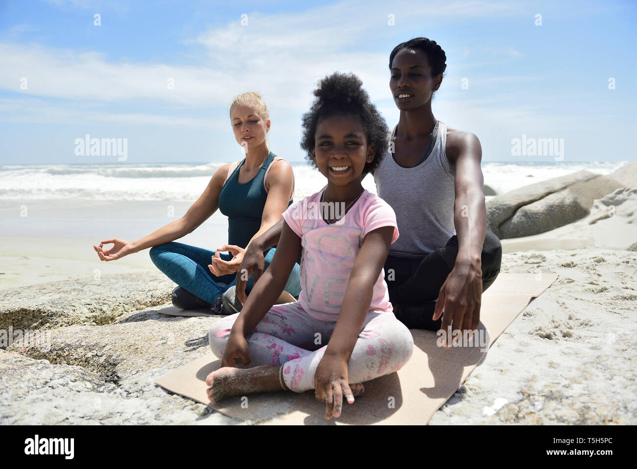Mother with daughter and friend doing a yoga exercise on the beach stock  photo