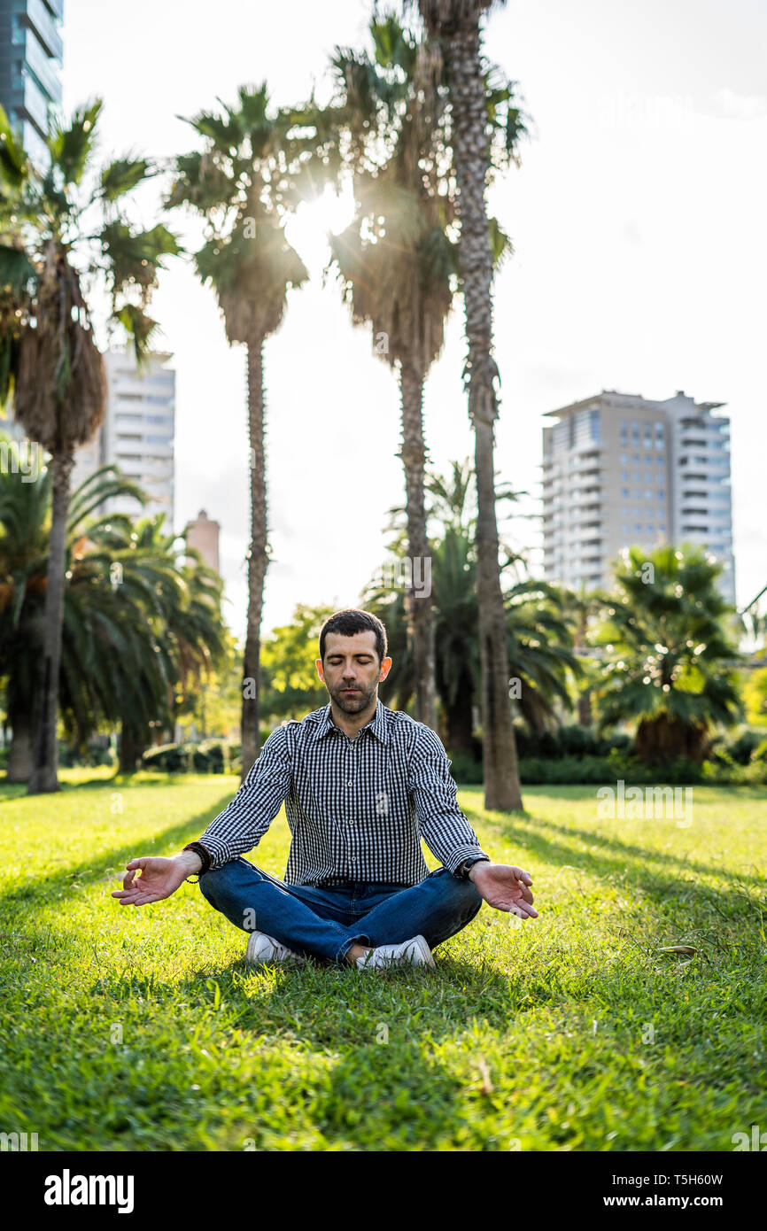 Man sitting on meadow in city park doing yoga exercise Stock Photo
