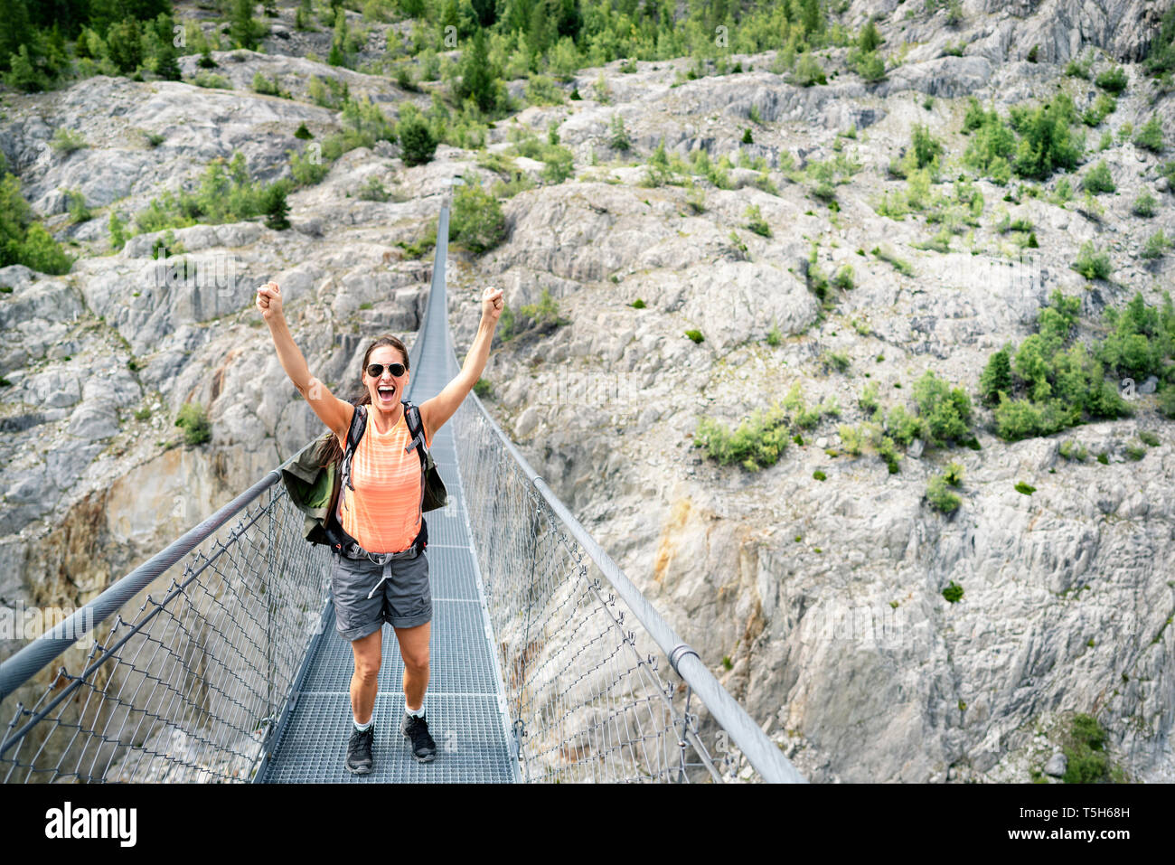 Switzerland, Valais, cheering woman on a hiking trip in the mountains from Belalp to Riederalp on a swinging bridge Stock Photo