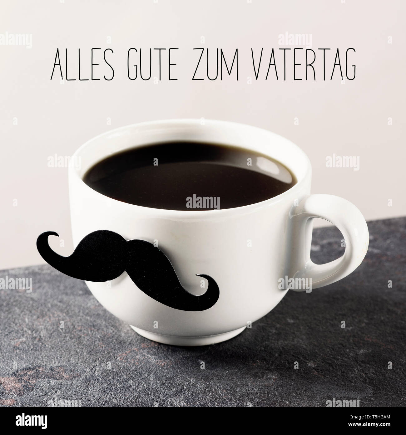 closeup of a white ceramic cup with coffee, with a mustache attached to it, and the text alles gute zum vatertag, happy fathers day written in german Stock Photo