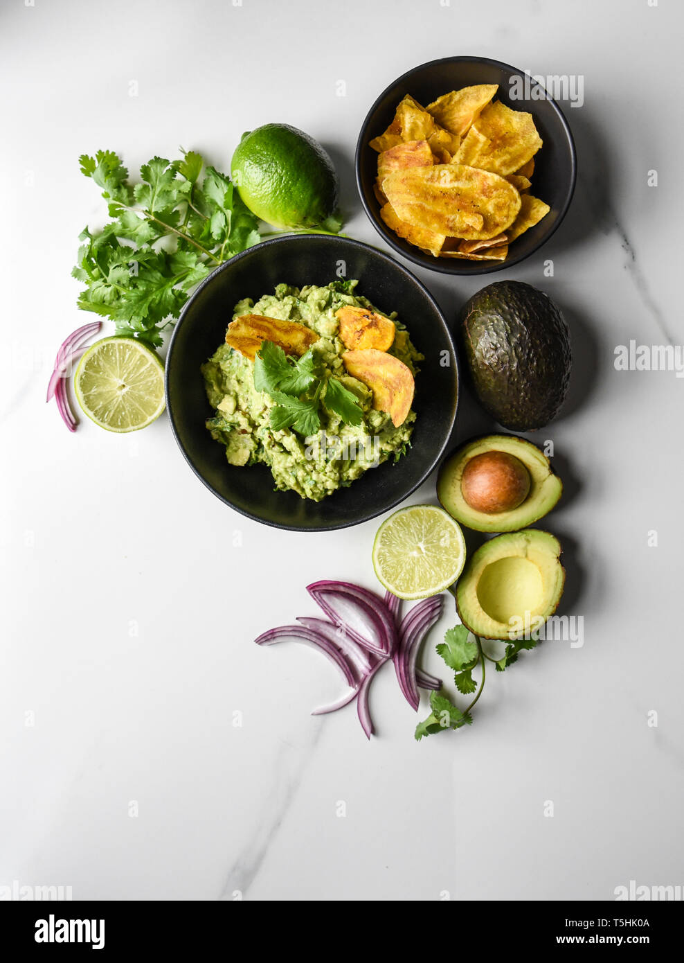 Bowl of guacamole and chips with it's ingredients on a marble counter. Stock Photo