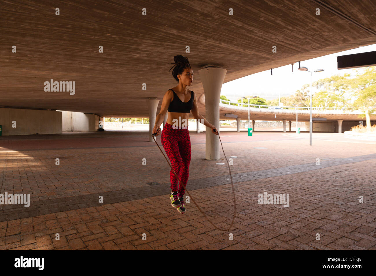 Young woman exercising with skipping rope under a bridge Stock Photo