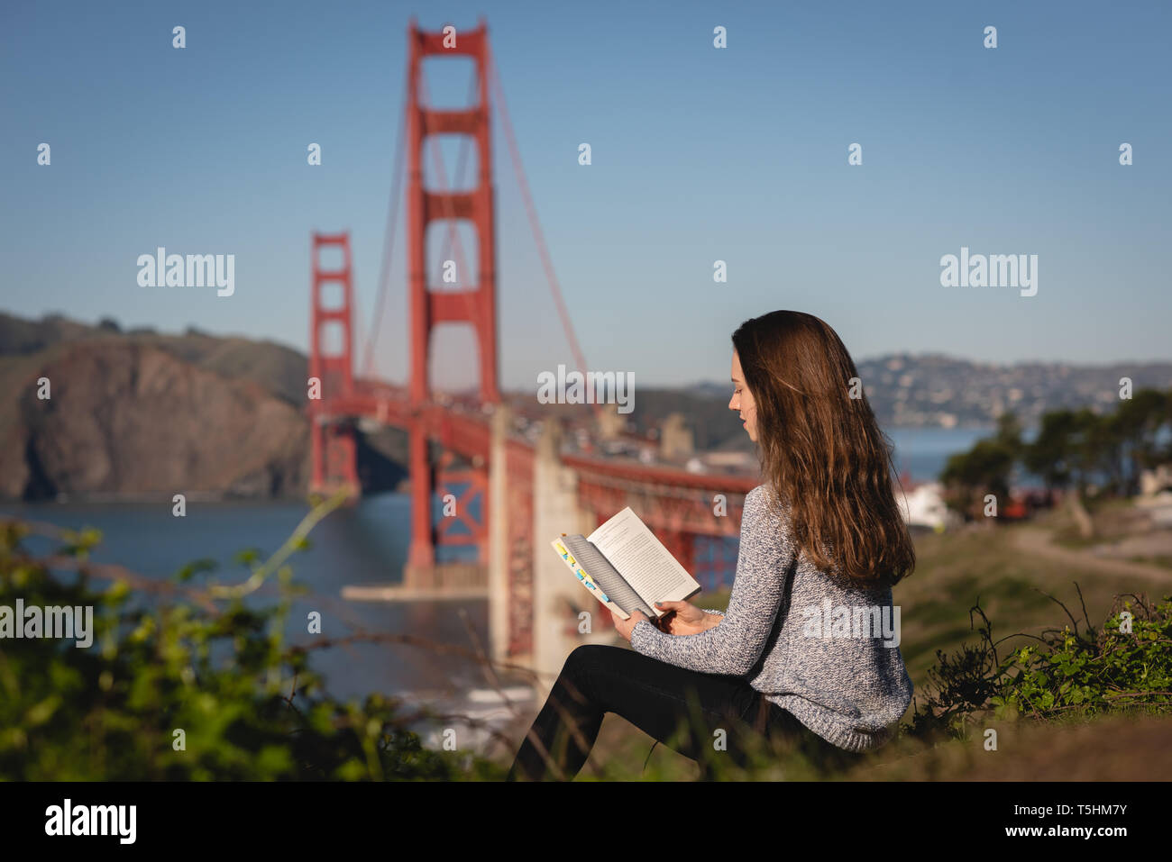 Beautiful woman reading book while sitting on mountain slope Stock Photo