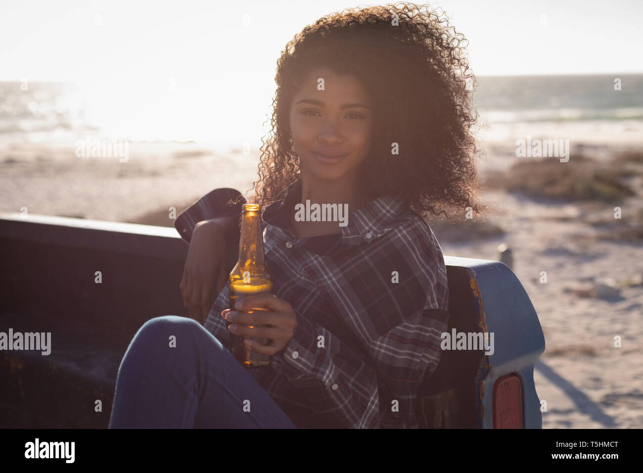 Beautiful woman sitting in car while having beer at beach Stock Photo