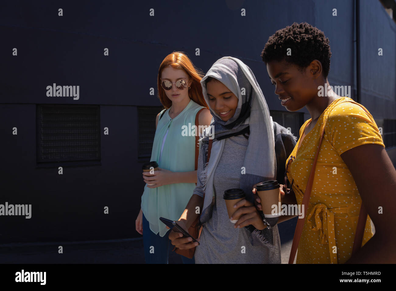 Female friends interacting with each other while walking in the city street Stock Photo