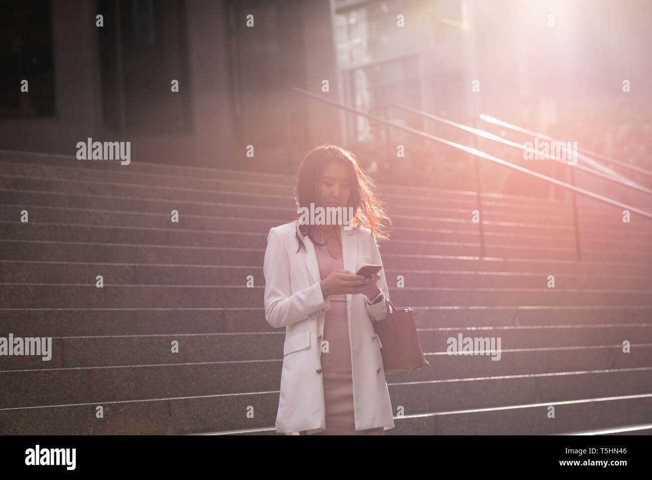 Woman using mobile phone while standing on stairs Stock Photo