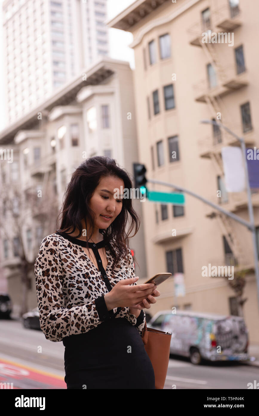 Beautiful woman using mobile phone while standing on street Stock Photo